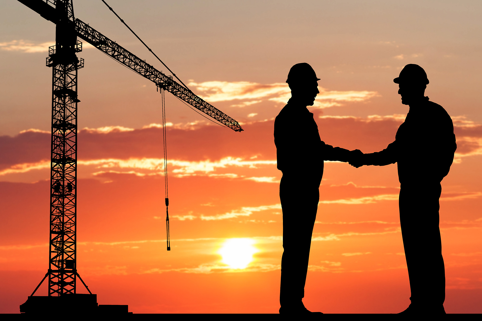 Construction Managing Director and Developer shaking hands on a construction site at sunset.