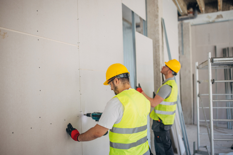 Two construction workers putting up accoustic wall panels in multi-residential construction